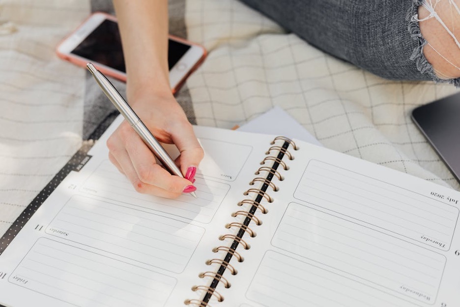 crop-woman-taking-notes-in-diary-while-sitting-in-park