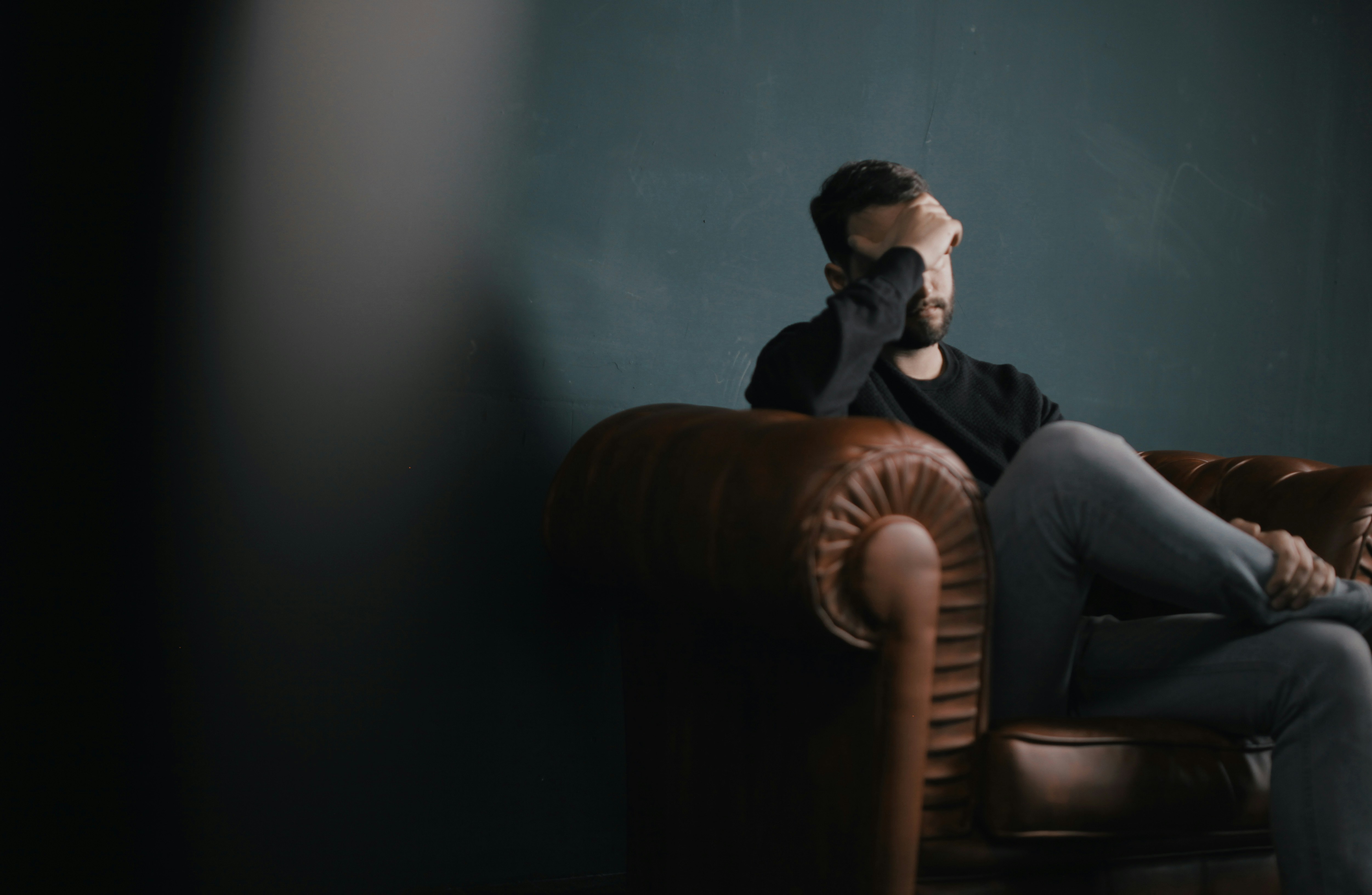 man-holds-his-head-while-sitting-on-a-sofa