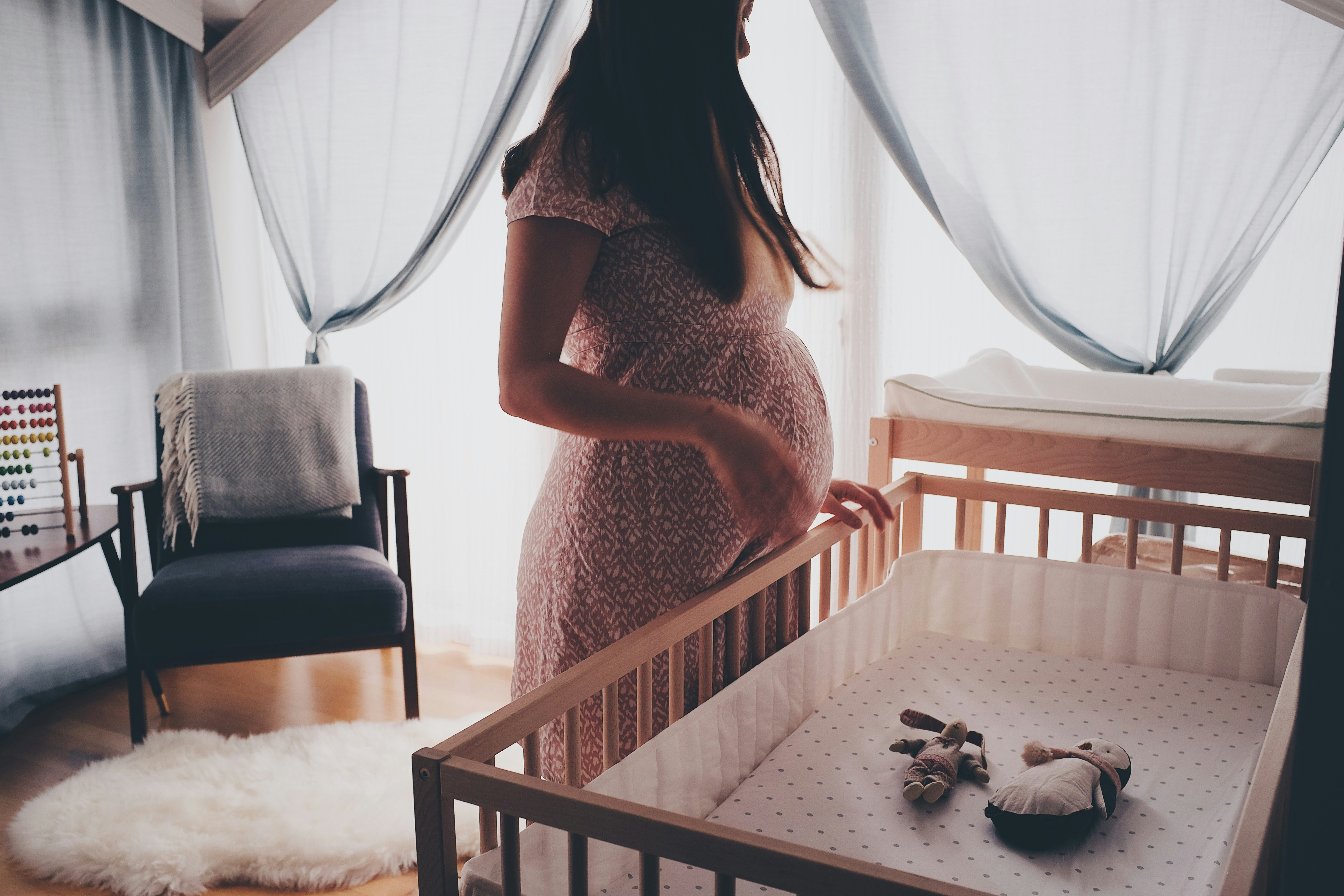 woman-in-white-lace-sleeveless-dress-standing-beside-brown-wooden-crib