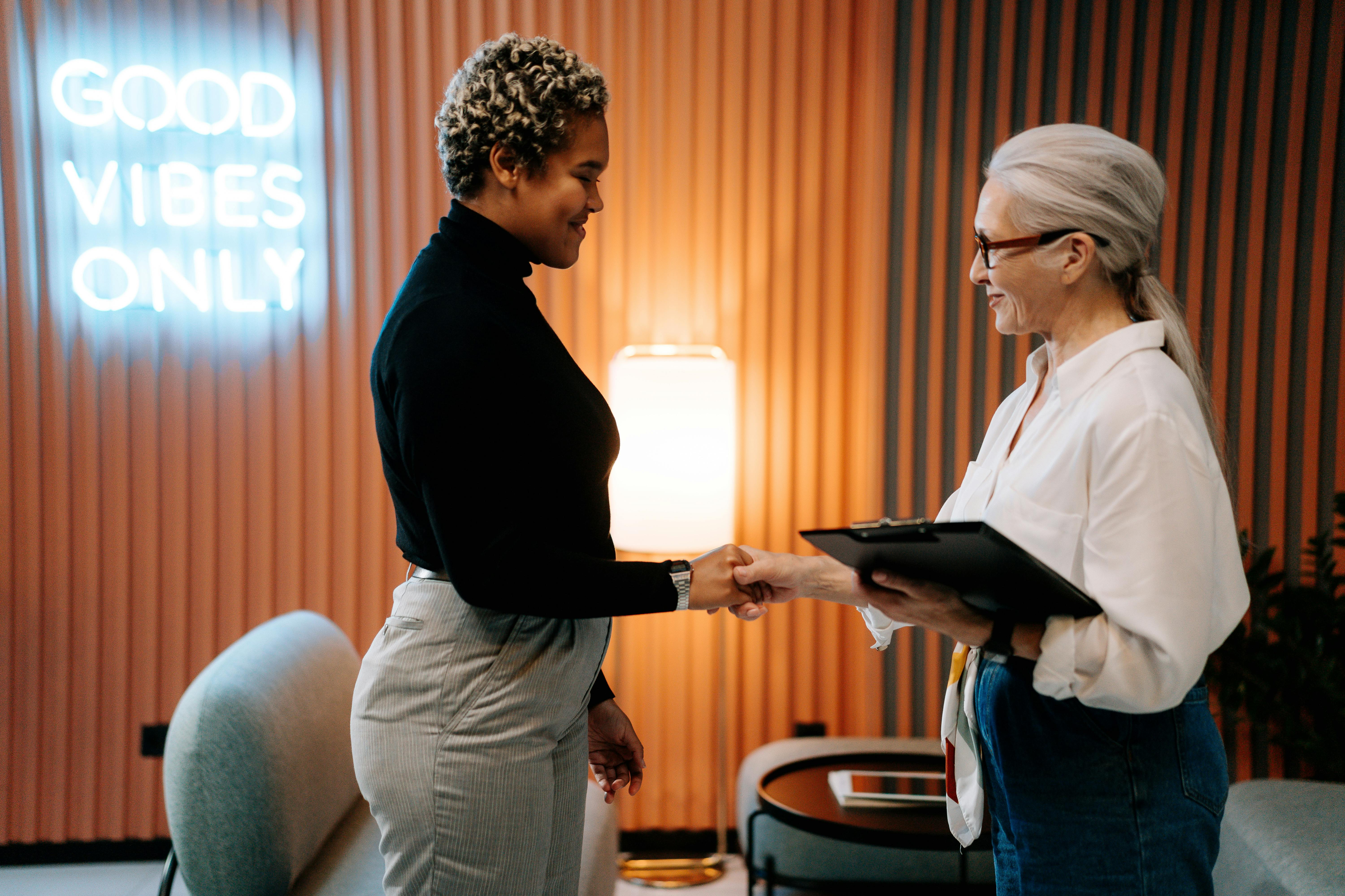 woman_in_black_shirt_shaking_hands_with_woman_in_white_shirt_holding_clipboard