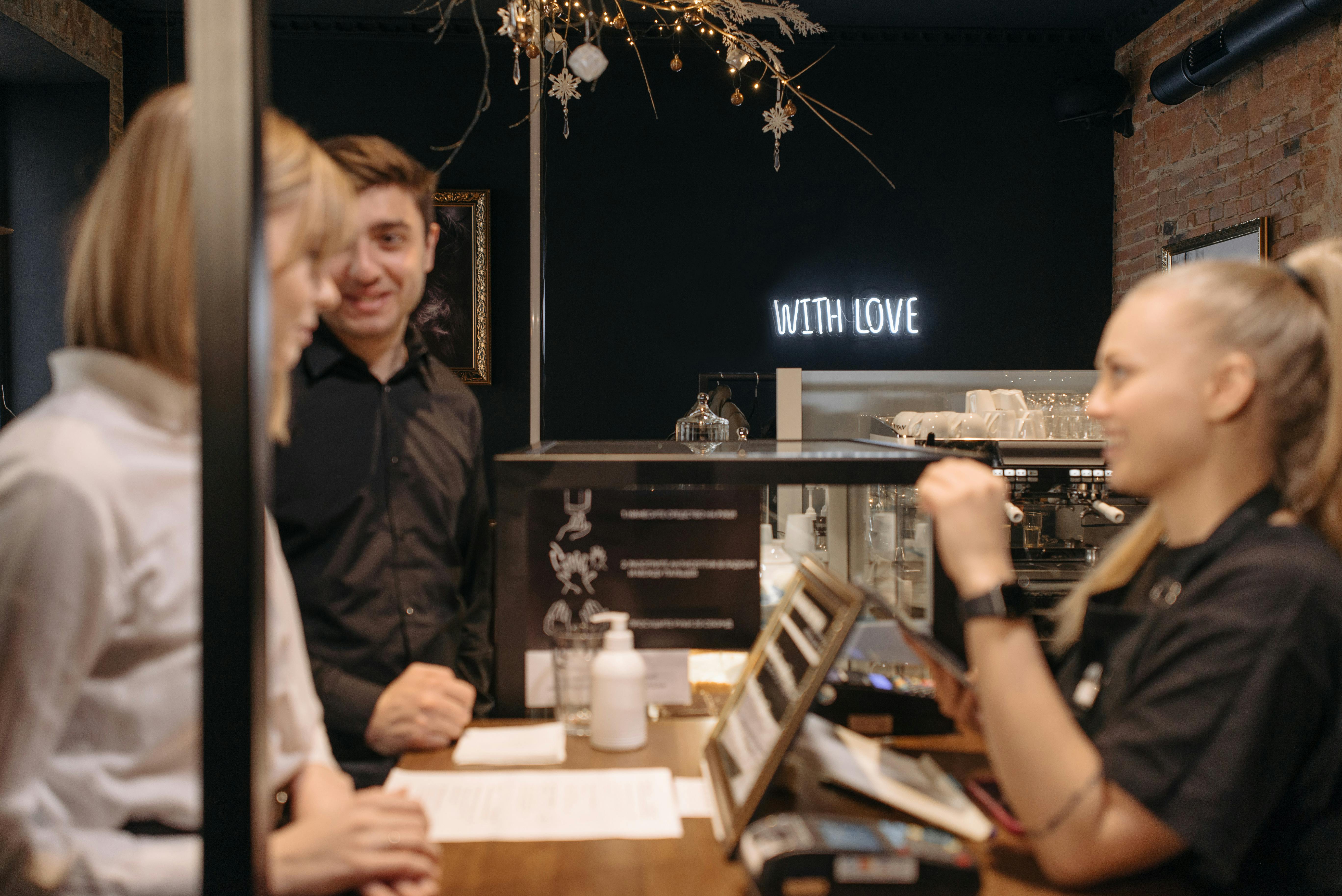 a-woman-in-black-shirt-talking-to-her-customers-while-ordering-at-the-counter