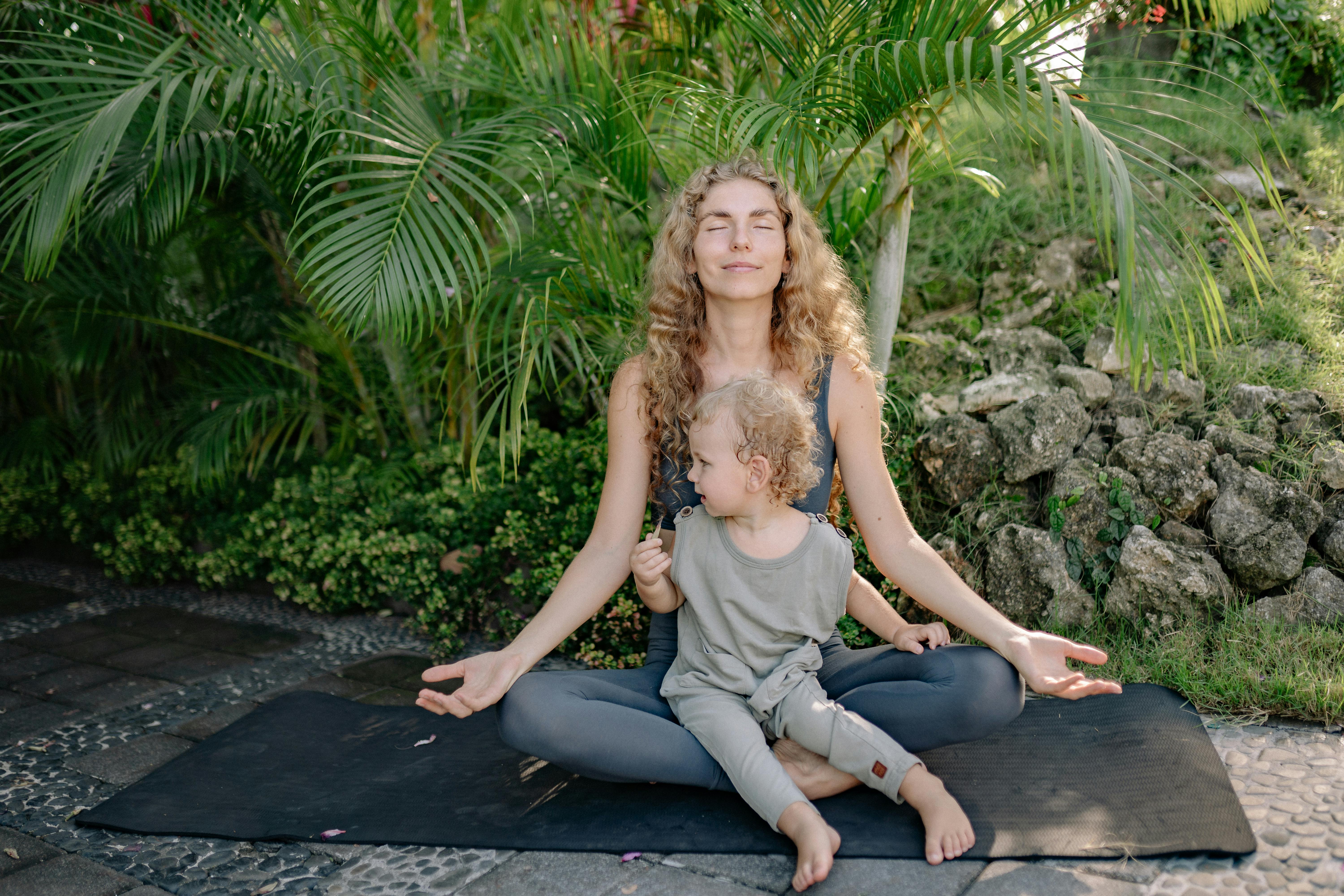 cheerful_sportswoman_meditating_in_lotus_pose_with_son